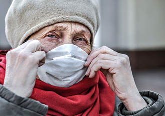 An elderly woman puts a respirator on her face - a protective mask against coronovirus infection. COVID-2019 Senior Health. The threat to the life of the elderly coronavirus